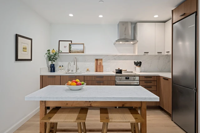 Freestanding wood-and-stone table-island with rush-seated stools, walnut Skinny Shaker base cabinets, hood and Smeg range behind