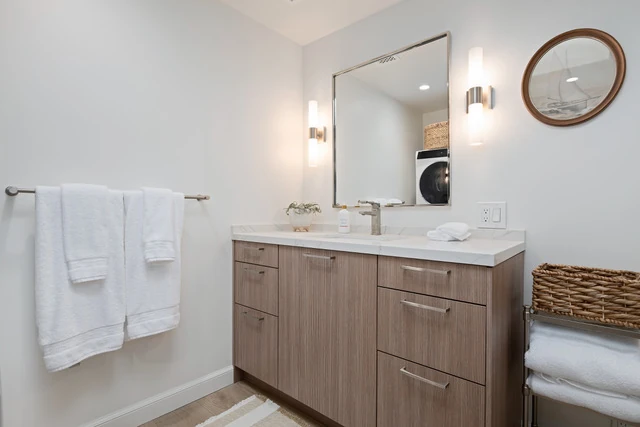 Primary bath vanity with fluted Pronorm front, sconces flanking the mirror, and a wall-mounted round secondary mirror
