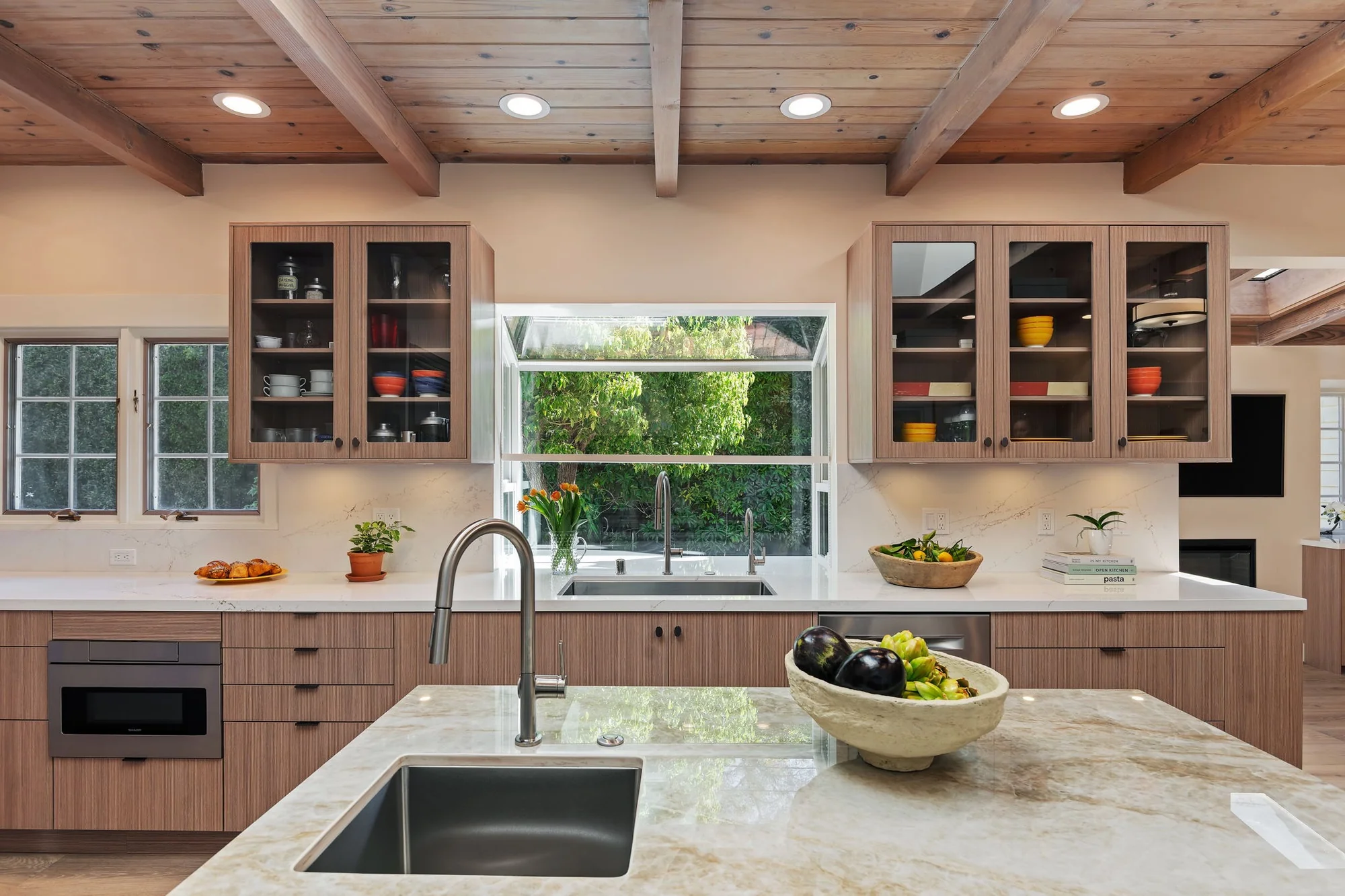 Garden window flanked by lit glass-front upper cabinets over the main sink